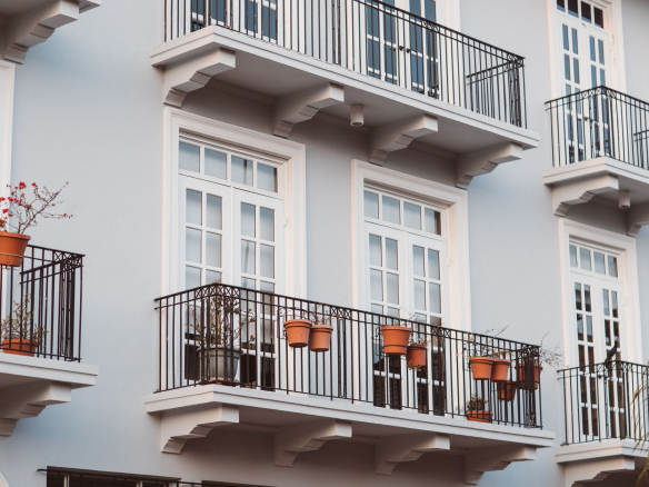 Front view of a modern building with balconies, pots, and white framed windows.