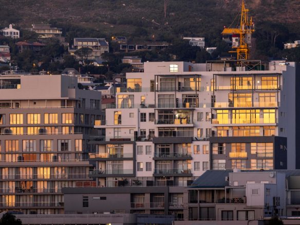 Urban residential buildings reflecting sunset light with a crane in the backdrop.