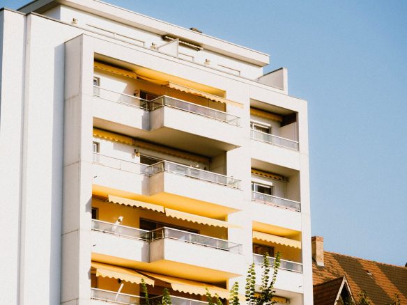 Low-angle view of a contemporary apartment building with yellow balconies against a clear sky.