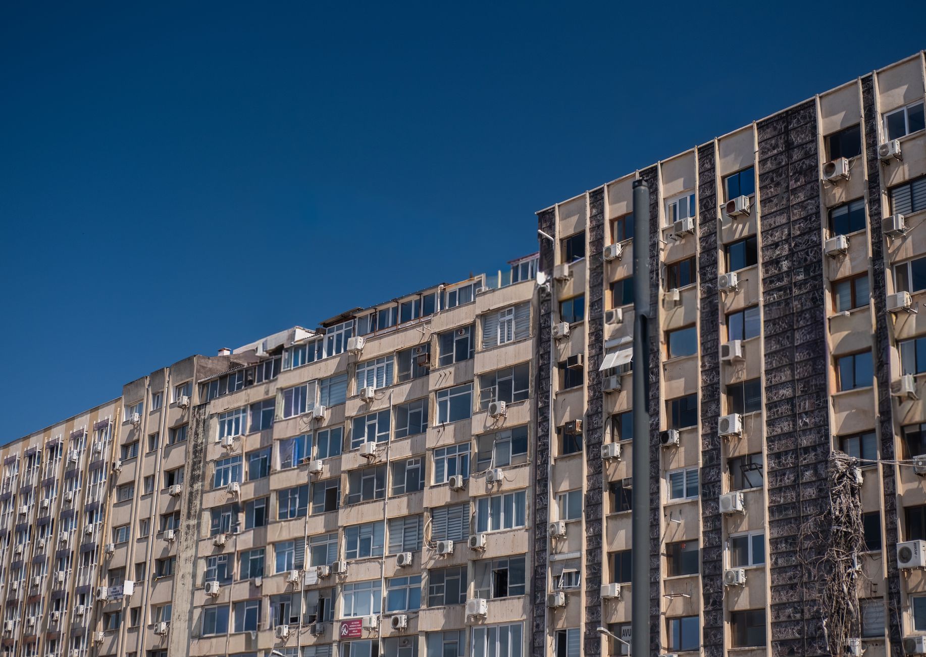 High-rise residential building with air conditioners in İzmir, Türkiye under a clear blue sky.